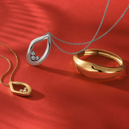 Brighton jewelry styled with gold and silver pendant necklaces and a gold-plated bangle bracelet on red fabric