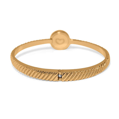 Brighton bangle bracelet with gold-plated ribbed band, round heart-engraved station, and crystal accent on a white background