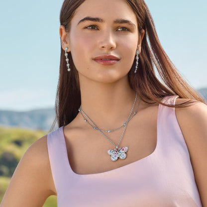 Model wearing a Brighton silver-plated butterfly pendant necklace with crystals and floral enamel, paired with crystal drop earrings
