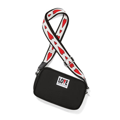 Brighton black crossbody handbag with red heart print strap and Love Brighton logo patch on a white background