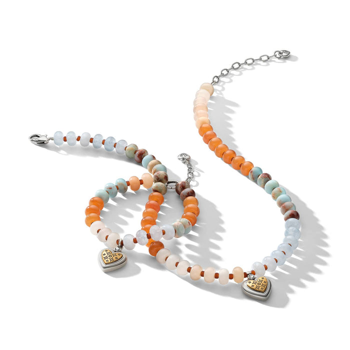 Brighton beaded necklace and bracelets with orange, blue, and cream stones and gold heart charms on a white background