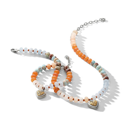 Brighton beaded necklace and bracelets with orange, blue, and cream stones and gold heart charms on a white background