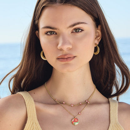 Model wearing Brighton gold-plated layered necklaces with crystal stations and enamel floral pendant, paired with gold hoop earrings